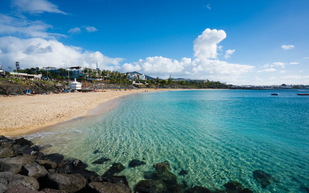 imagen de playa blanca, mar y arena con pueblo de fondo